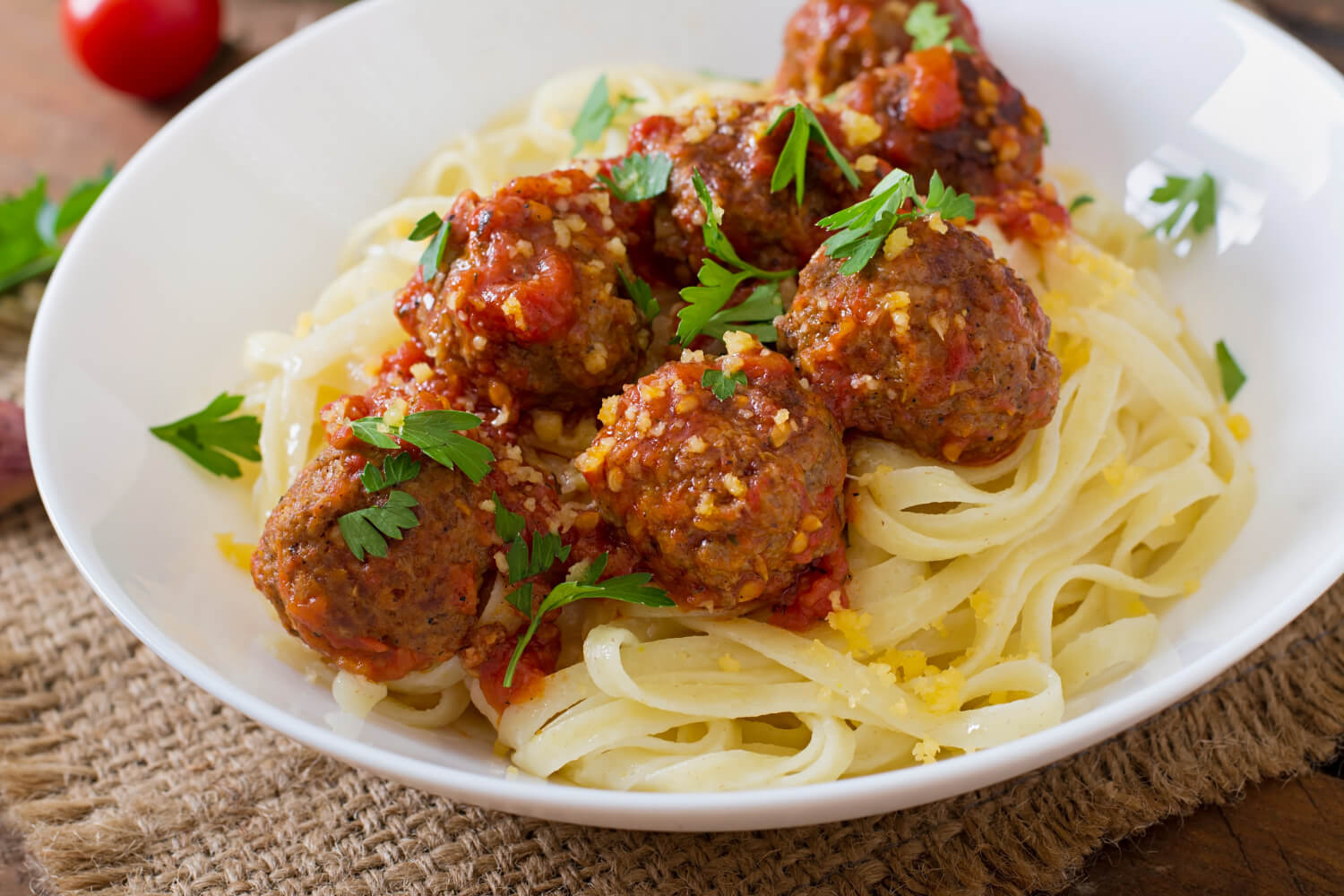 Italian meatballs served in rich tomato sauce, garnished with herbs, on a white plate. 