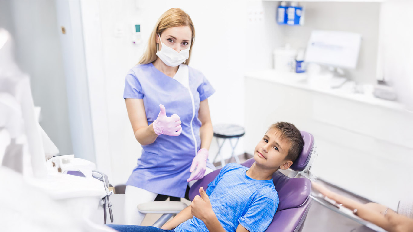 young female dentist and boy gesturing thumbs up in clinic expanded