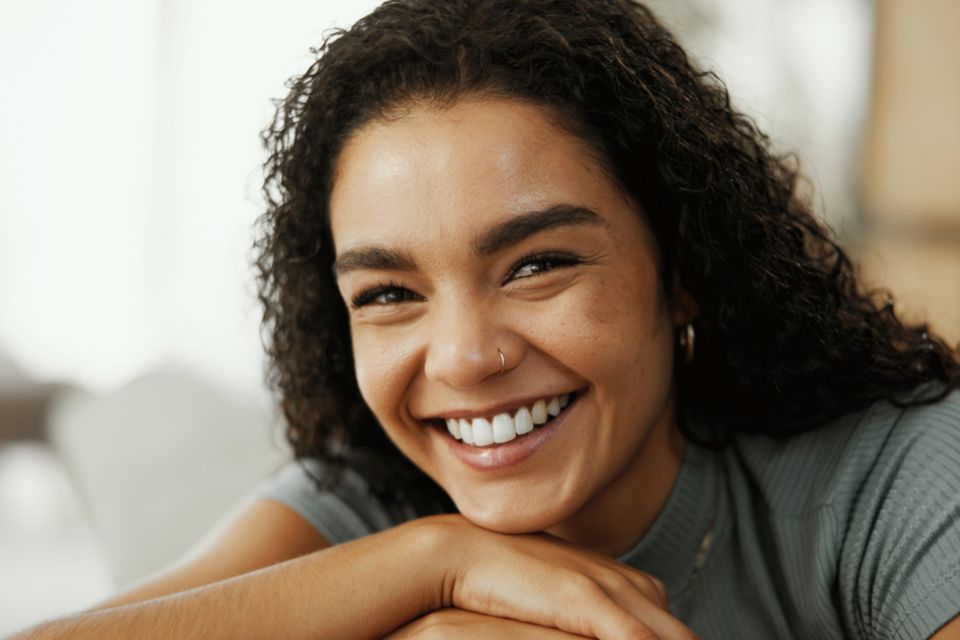 A woman smiles while sitting comfortably on a couch, exuding warmth and happiness.