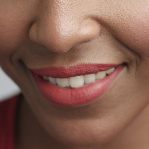 Close-up of a person smiling, with red lipstick and visible white teeth. The skin has a warm tone, conveying a cheerful and friendly mood.