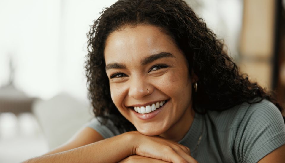A woman smiles while sitting comfortably on a couch, exuding warmth and happiness.